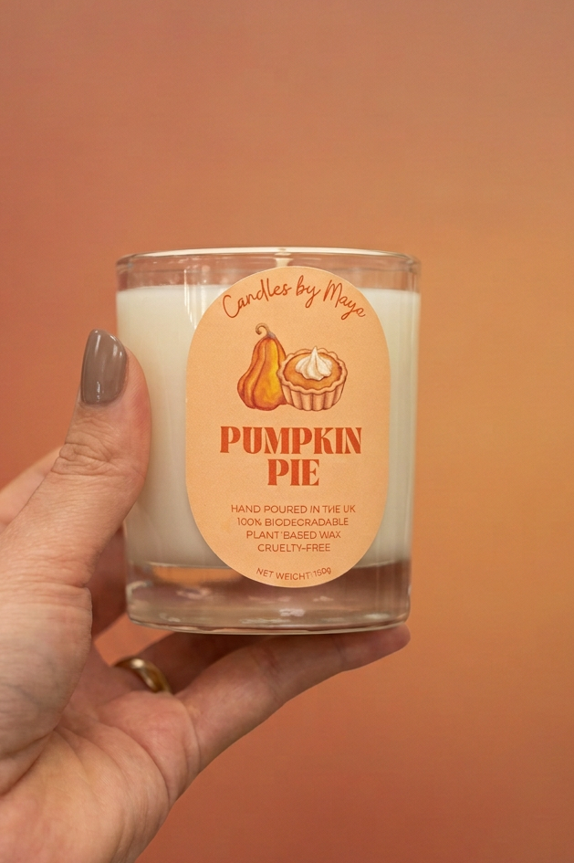 Pumpkin Pie Classic candle held in a hand with taupe-brown nail polish against a warm terracotta studio background