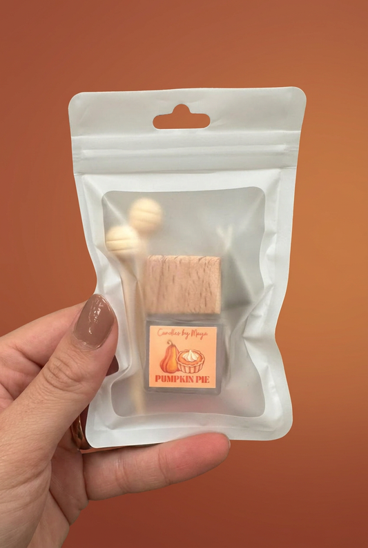 Pumpkin Pie car diffuser in its original pouch held in a hand against a soft terracotta studio background