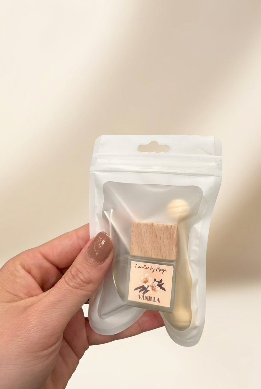 Vanilla car diffuser in its original pouch held in a hand against a soft cream studio background