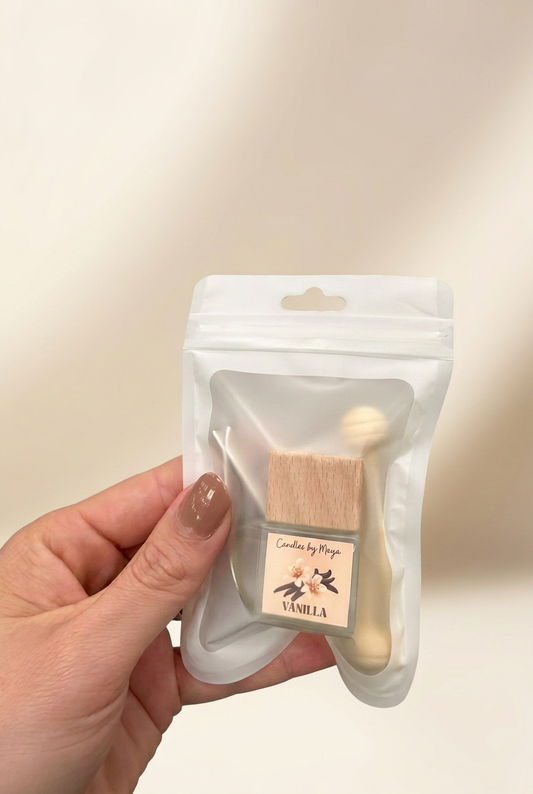 Vanilla car diffuser in its original pouch held in a hand against a soft cream studio background