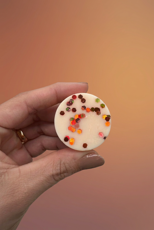 Pumpkin Pie wax melt with colourful decorations held in a hand against a warm terracotta studio background